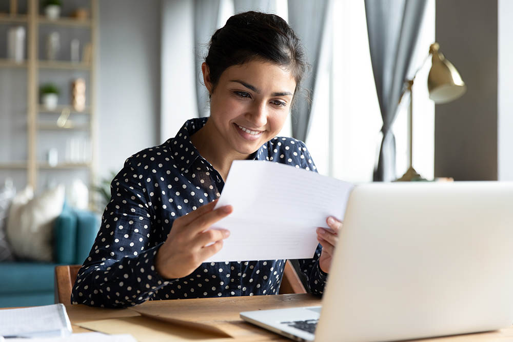 Smiling woman holding energy bill letter sitting at table