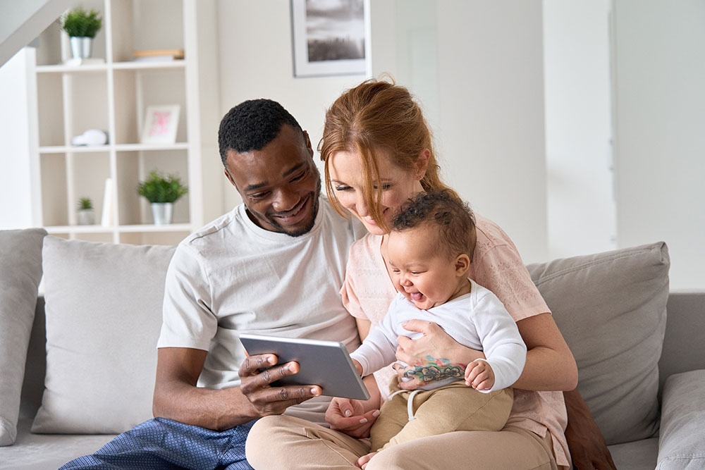 Installation Protections – Action of Energy Cambridgeshire Happy young family couple holding daughter having fun with digital tablet sitting on sofa