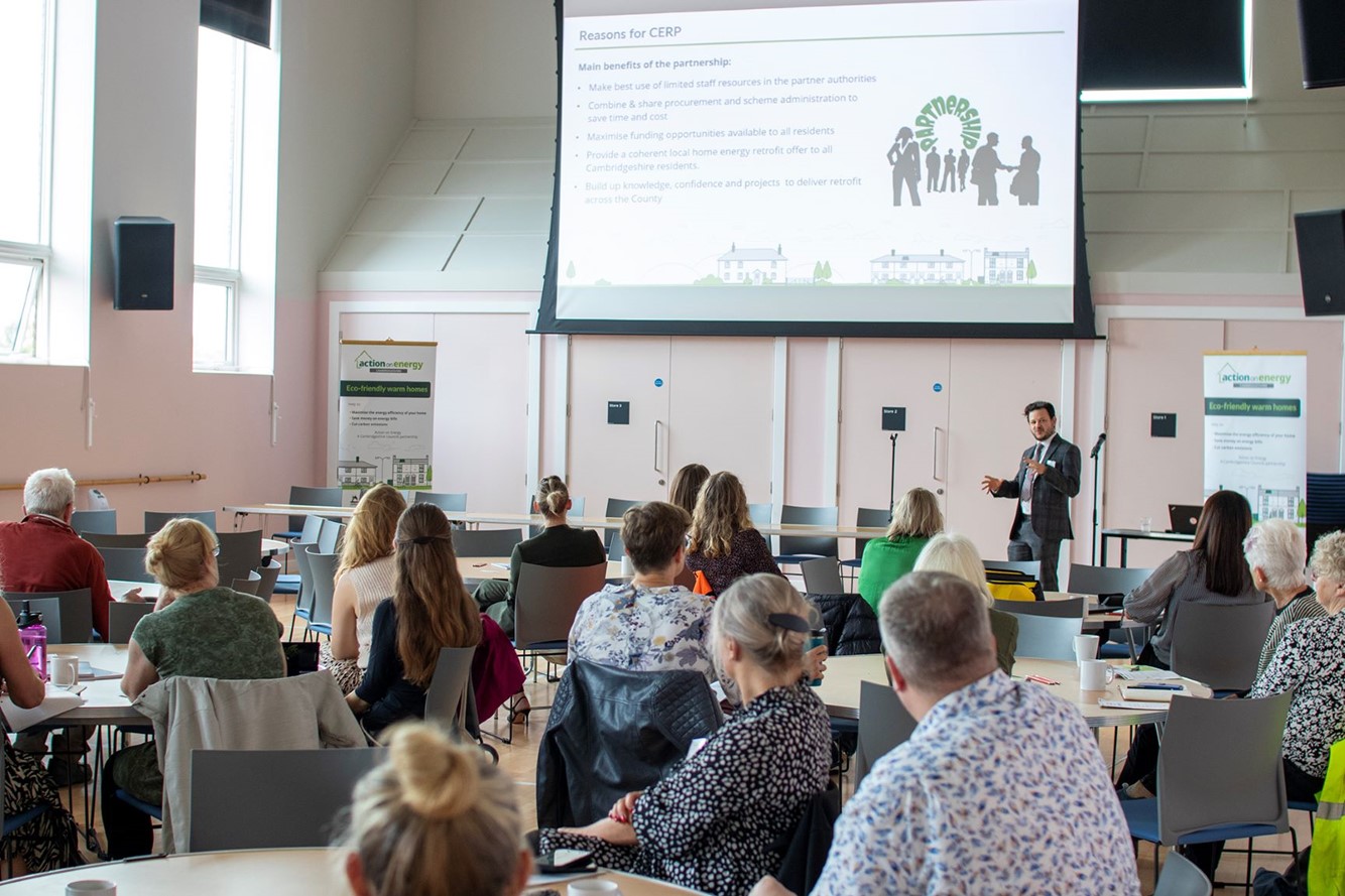 A picture of the Action on Energy Event showing an Action on Energy staff member speaking to attendees with a slideshow